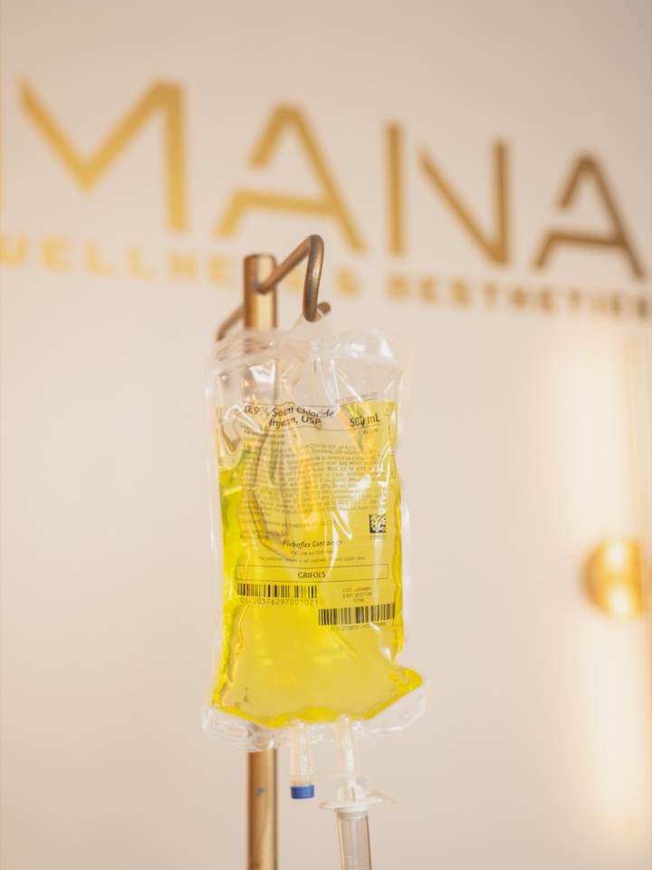 An IV infusion bag hanging on a stand in front of the illuminated Mana wall sign