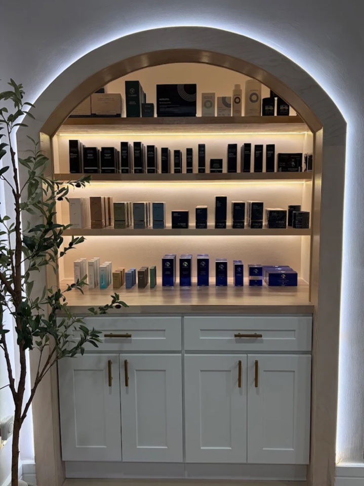 Medical-grade skincare on lit shelves in an arched alcove at the practice
