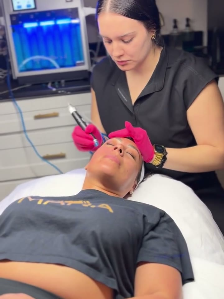 A clinician standing over a patient reclined in a treatment chair, working on her face with a handheld device